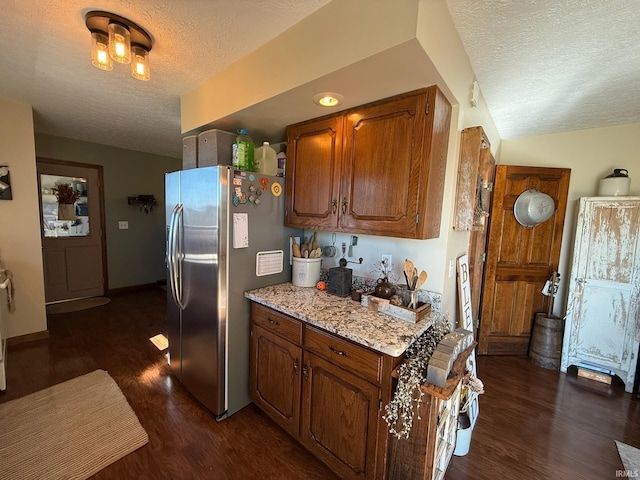 kitchen with light stone counters, a textured ceiling, stainless steel refrigerator, and dark hardwood / wood-style flooring