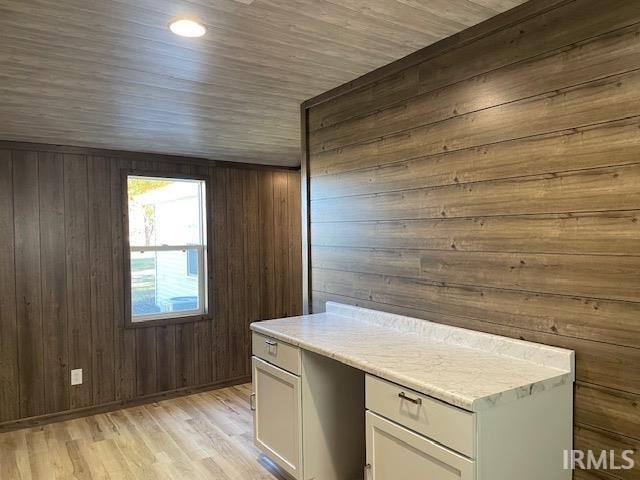 kitchen featuring light hardwood / wood-style floors, white cabinetry, and wooden walls