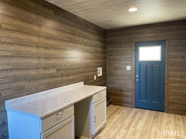 interior space featuring light hardwood / wood-style floors, wood walls, white cabinets, and light stone countertops