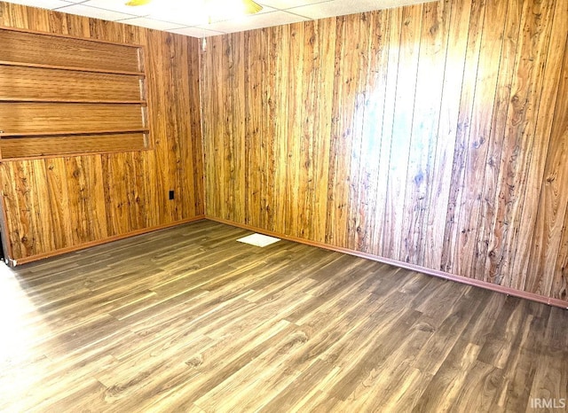 spare room featuring a paneled ceiling, wooden walls, and dark hardwood / wood-style floors