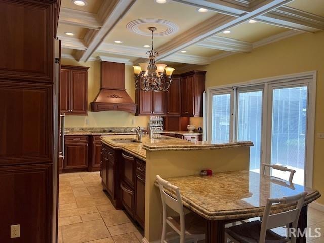 kitchen with custom exhaust hood, an island with sink, beamed ceiling, pendant lighting, and coffered ceiling