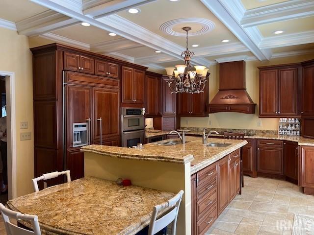 kitchen featuring custom exhaust hood, beam ceiling, hanging light fixtures, a kitchen breakfast bar, and a chandelier