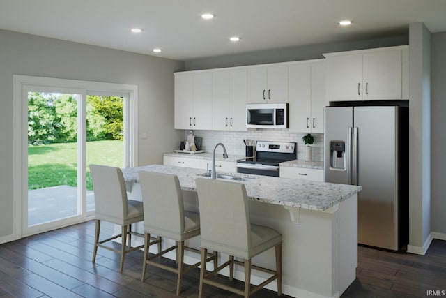 kitchen with white cabinetry, sink, stainless steel appliances, dark hardwood / wood-style flooring, and an island with sink