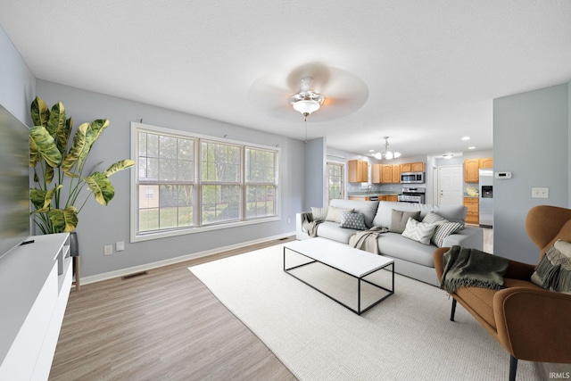 living room with ceiling fan with notable chandelier and light wood-type flooring