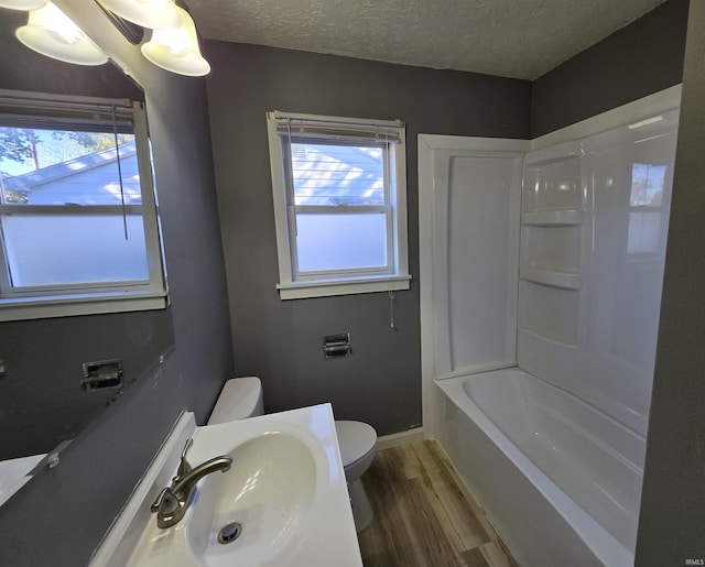 full bathroom featuring hardwood / wood-style floors, a textured ceiling, toilet, sink, and washtub / shower combination