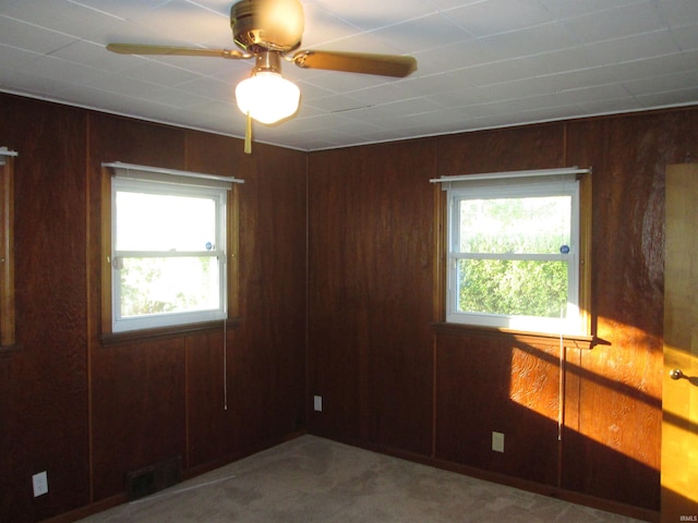 carpeted empty room with wood walls, a wealth of natural light, and ceiling fan