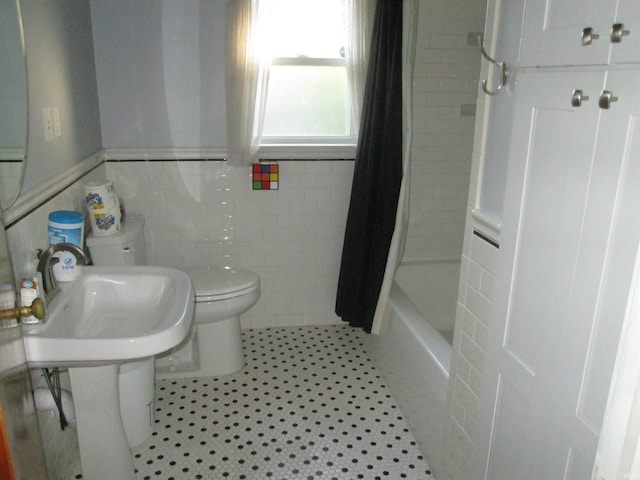 bathroom with a wainscoted wall, shower / bath combo with shower curtain, toilet, and tile walls