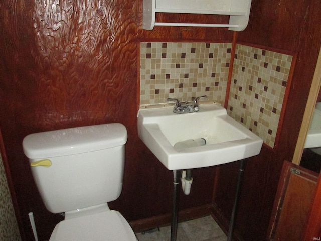 half bath with backsplash, toilet, and a sink