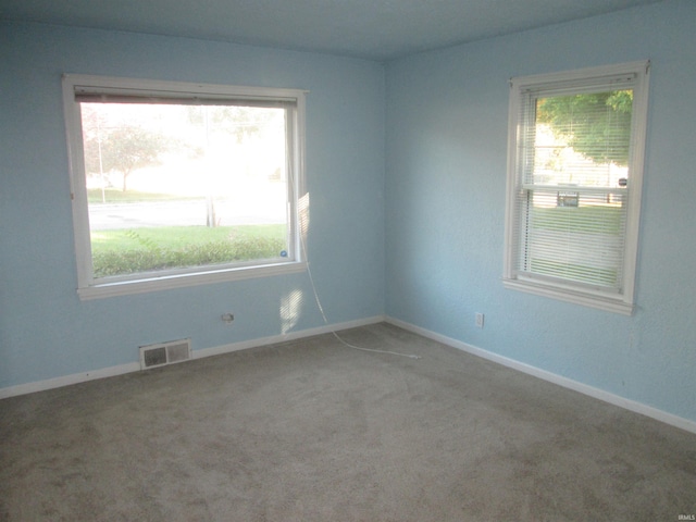 carpeted empty room with baseboards, a wealth of natural light, and visible vents