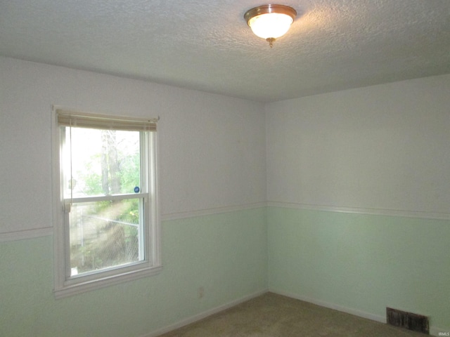 carpeted spare room with visible vents, a textured ceiling, and baseboards