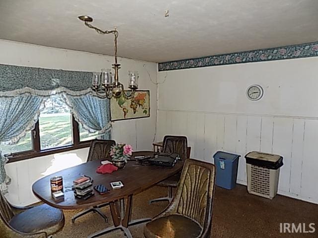 dining space featuring wood walls, a chandelier, and dark carpet