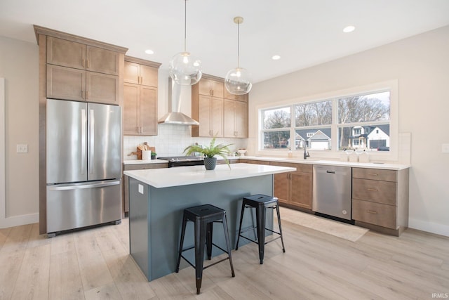 kitchen with a center island, stainless steel appliances, wall chimney exhaust hood, decorative light fixtures, and light hardwood / wood-style flooring