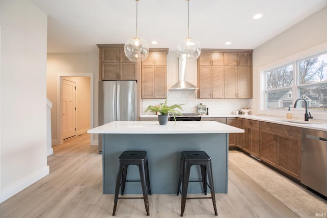 kitchen featuring wall chimney range hood, appliances with stainless steel finishes, sink, a kitchen island, and light hardwood / wood-style floors