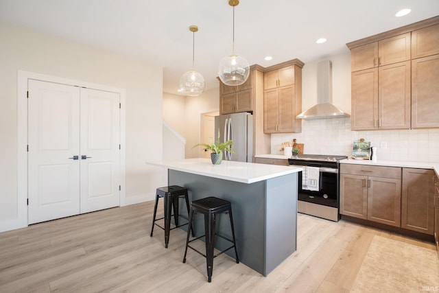 kitchen with a kitchen island, wall chimney exhaust hood, hanging light fixtures, appliances with stainless steel finishes, and light hardwood / wood-style floors