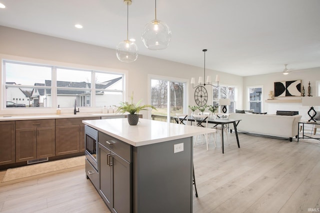 kitchen with pendant lighting, stainless steel microwave, sink, and light wood-type flooring