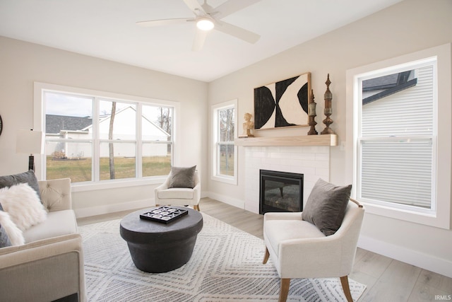 living room with a fireplace, light wood-type flooring, and ceiling fan