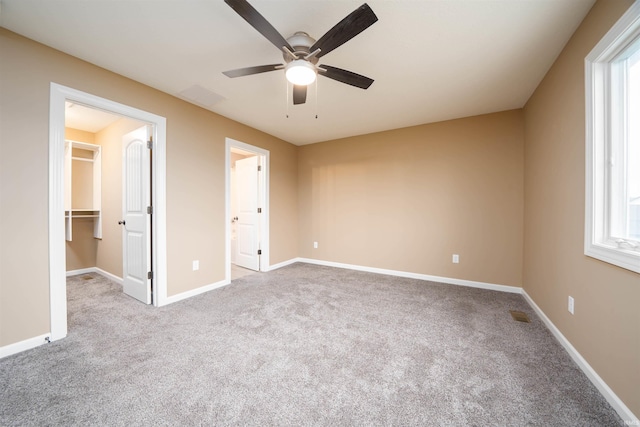 unfurnished bedroom featuring a walk in closet, a closet, light colored carpet, and ceiling fan