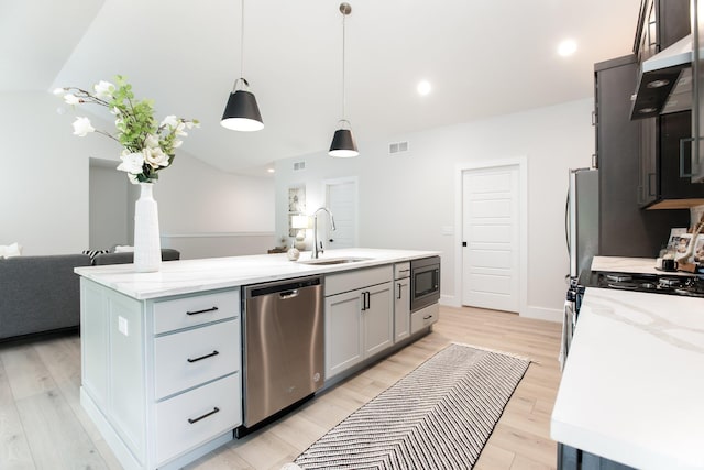 kitchen with appliances with stainless steel finishes, hanging light fixtures, light hardwood / wood-style floors, gray cabinets, and a kitchen island with sink