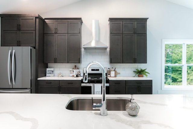 kitchen with lofted ceiling, wall chimney range hood, sink, stainless steel refrigerator, and tasteful backsplash