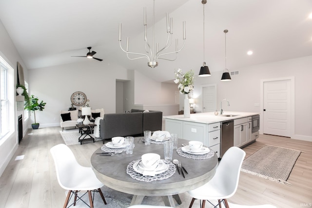 dining space featuring sink, vaulted ceiling, ceiling fan with notable chandelier, and light wood-type flooring