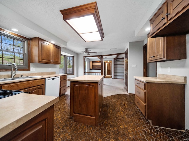 kitchen featuring ceiling fan, a kitchen island, a textured ceiling, dishwasher, and sink