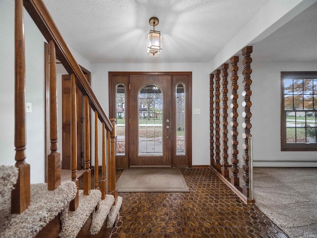 entrance foyer featuring a textured ceiling, dark carpet, and plenty of natural light