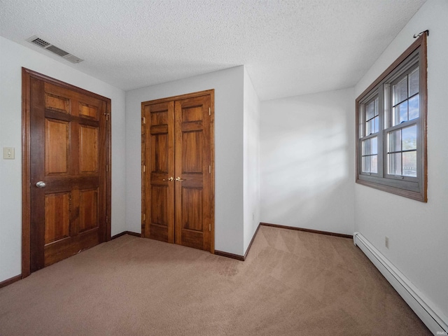 unfurnished bedroom featuring baseboard heating, a textured ceiling, light colored carpet, and a closet