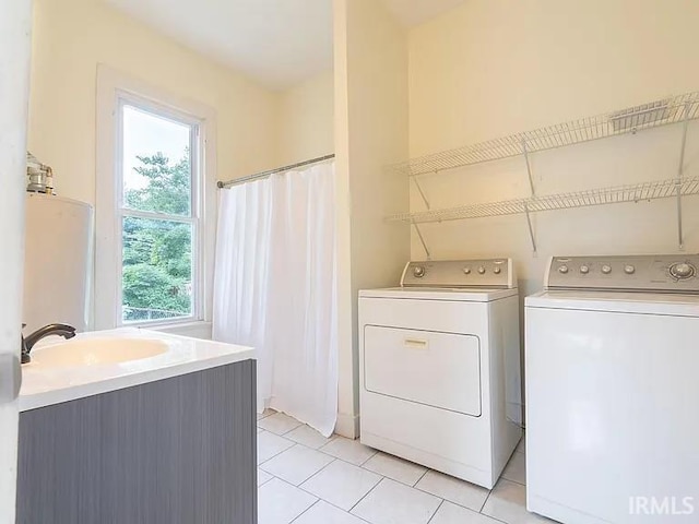 laundry area with sink, washing machine and clothes dryer, a healthy amount of sunlight, and light tile patterned floors