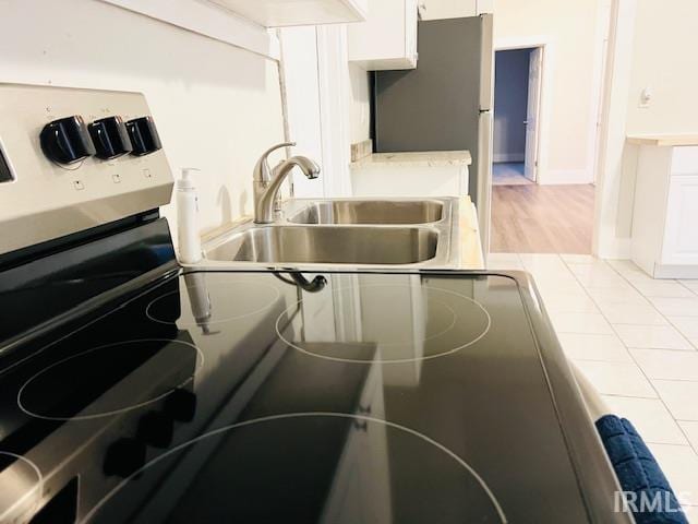 details with white cabinets, sink, light wood-type flooring, and stainless steel refrigerator