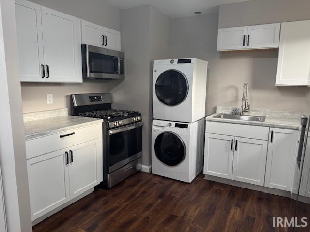 kitchen with white cabinets, stacked washer / drying machine, stainless steel appliances, and sink