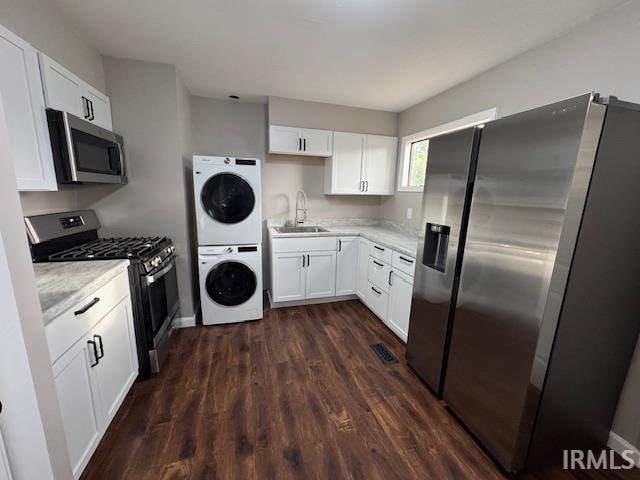 kitchen featuring stacked washer / drying machine, sink, white cabinets, appliances with stainless steel finishes, and dark hardwood / wood-style flooring