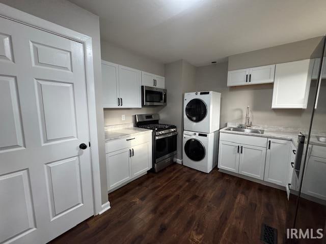 kitchen with dark hardwood / wood-style floors, appliances with stainless steel finishes, sink, white cabinets, and stacked washer / dryer