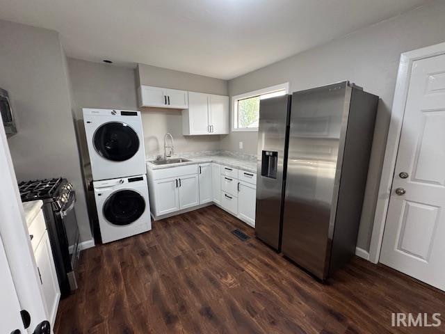 kitchen with appliances with stainless steel finishes, sink, stacked washer / dryer, white cabinets, and dark wood-type flooring