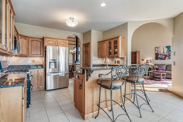 kitchen with appliances with stainless steel finishes, a kitchen breakfast bar, dark stone counters, a notable chandelier, and light tile patterned floors