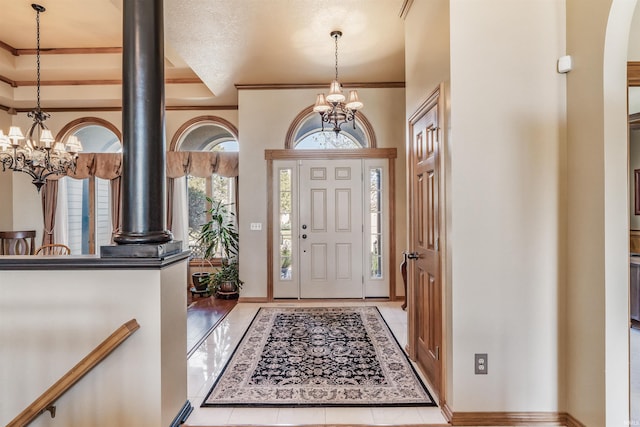 tiled entrance foyer with ornate columns, ornamental molding, a raised ceiling, a chandelier, and a textured ceiling