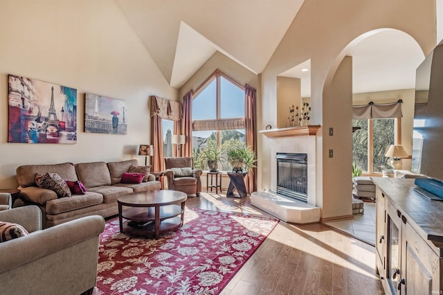 living room featuring high vaulted ceiling, a fireplace, and light wood-type flooring