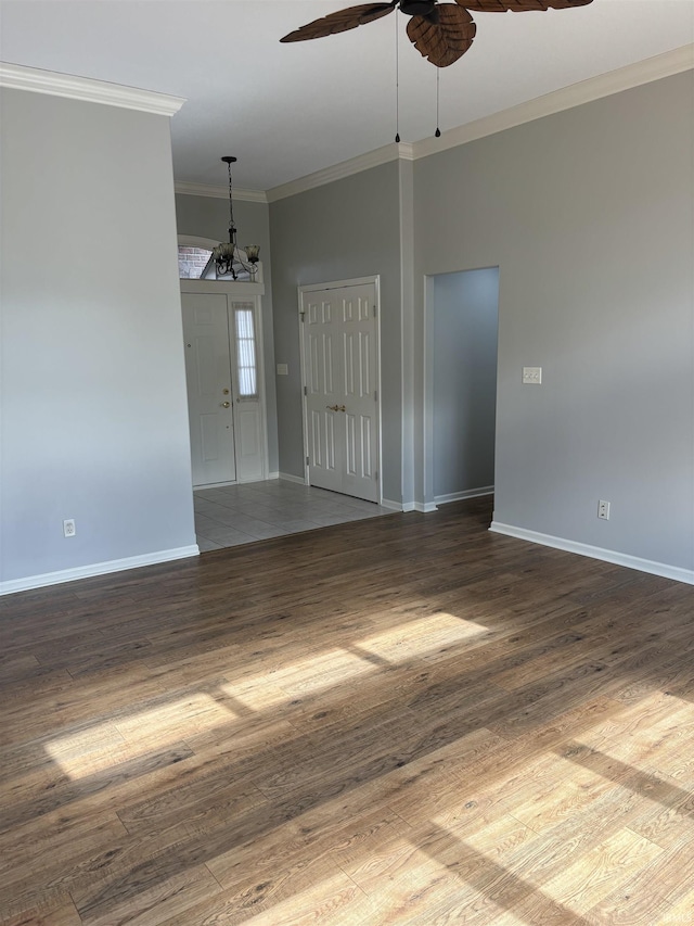 empty room with ornamental molding, dark hardwood / wood-style floors, and ceiling fan with notable chandelier