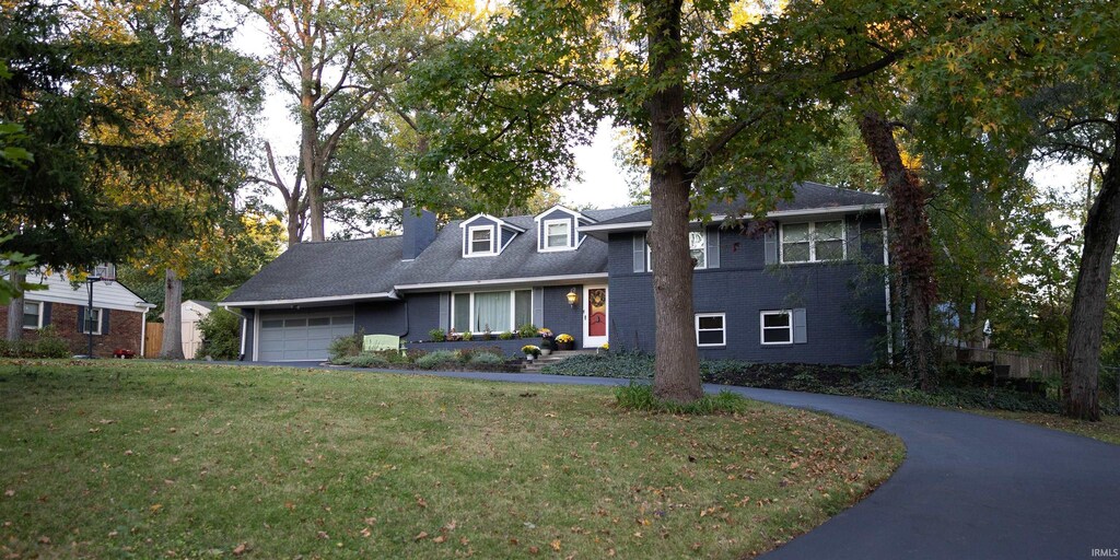 view of front facade with a chimney, a front yard, a garage, brick siding, and aphalt driveway