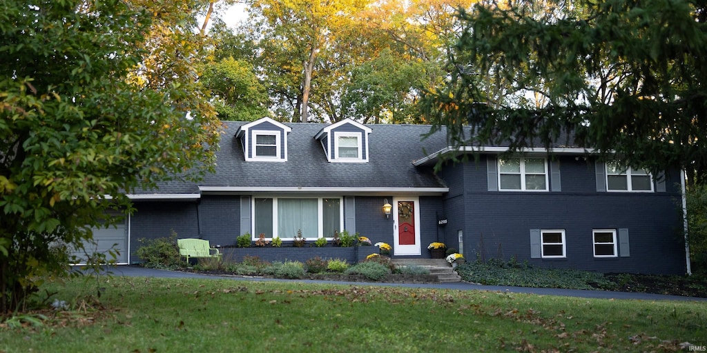 tri-level home with brick siding, a garage, a front yard, and a shingled roof