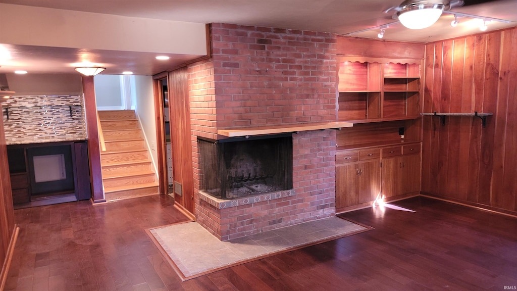 unfurnished living room with wood walls, a brick fireplace, and dark hardwood / wood-style flooring