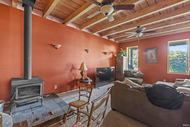 living room featuring beamed ceiling, wood ceiling, a wood stove, and ceiling fan