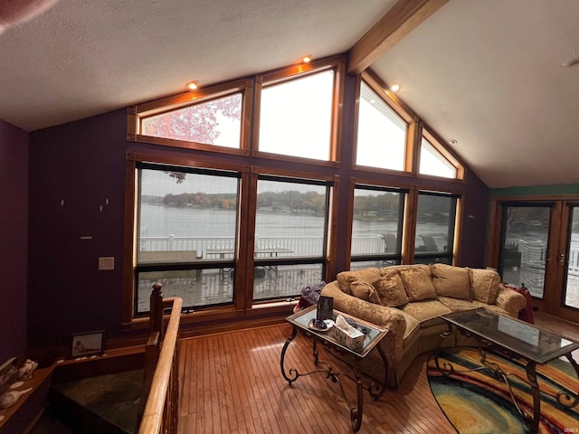 living room with a textured ceiling, lofted ceiling with beams, a water view, and wood-type flooring