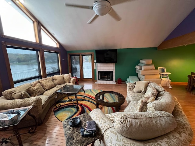 living room featuring lofted ceiling, hardwood / wood-style flooring, a tile fireplace, and ceiling fan