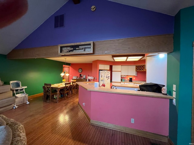 kitchen featuring kitchen peninsula, hardwood / wood-style floors, hanging light fixtures, white fridge with ice dispenser, and vaulted ceiling