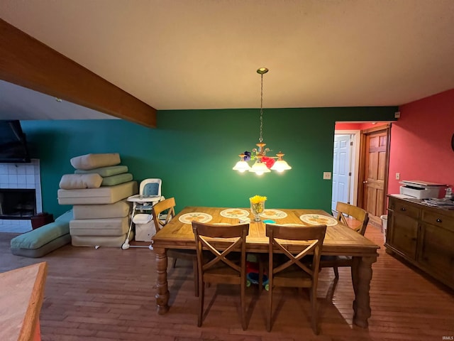 dining area featuring a tiled fireplace, hardwood / wood-style flooring, and beam ceiling