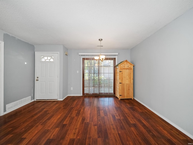 interior space with dark wood-type flooring, a notable chandelier, and a textured ceiling