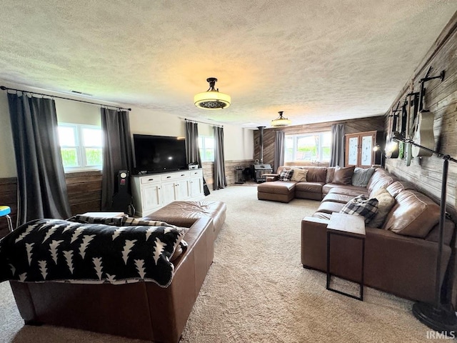 carpeted living room with wooden walls, a textured ceiling, and plenty of natural light