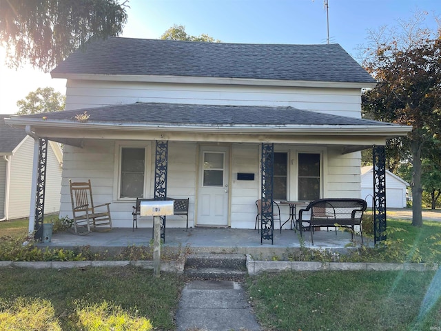 bungalow-style home with covered porch, a shingled roof, and a front yard