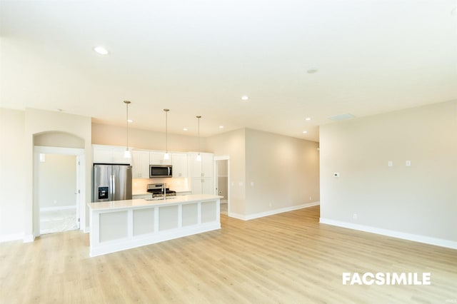 kitchen featuring appliances with stainless steel finishes, light wood-type flooring, white cabinetry, decorative light fixtures, and a center island with sink