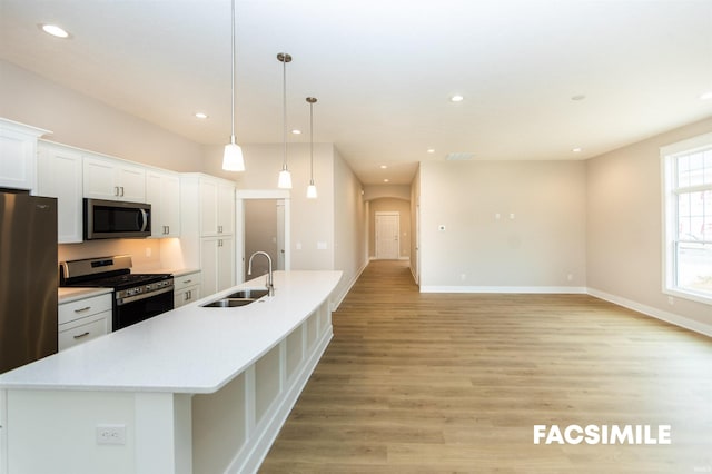 kitchen with a center island with sink, sink, pendant lighting, white cabinetry, and appliances with stainless steel finishes